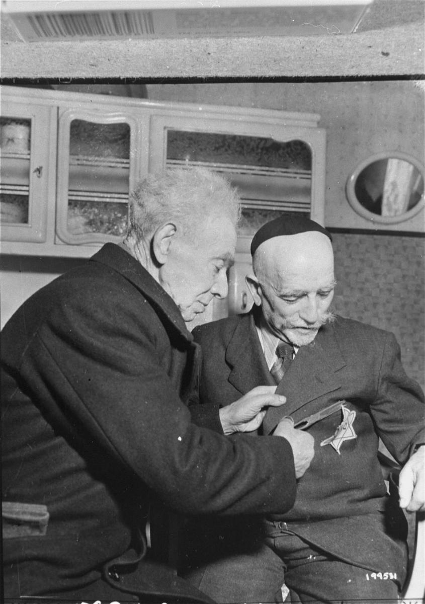 סיימון טרמפטר בן ה-83 מסיר את הטלאי הצהוב מהחליפה של ידידו ג‘וסף קלר, 27 בינואר 1945. קירקייד (לימבורג), הולנד. צילום: USHMM